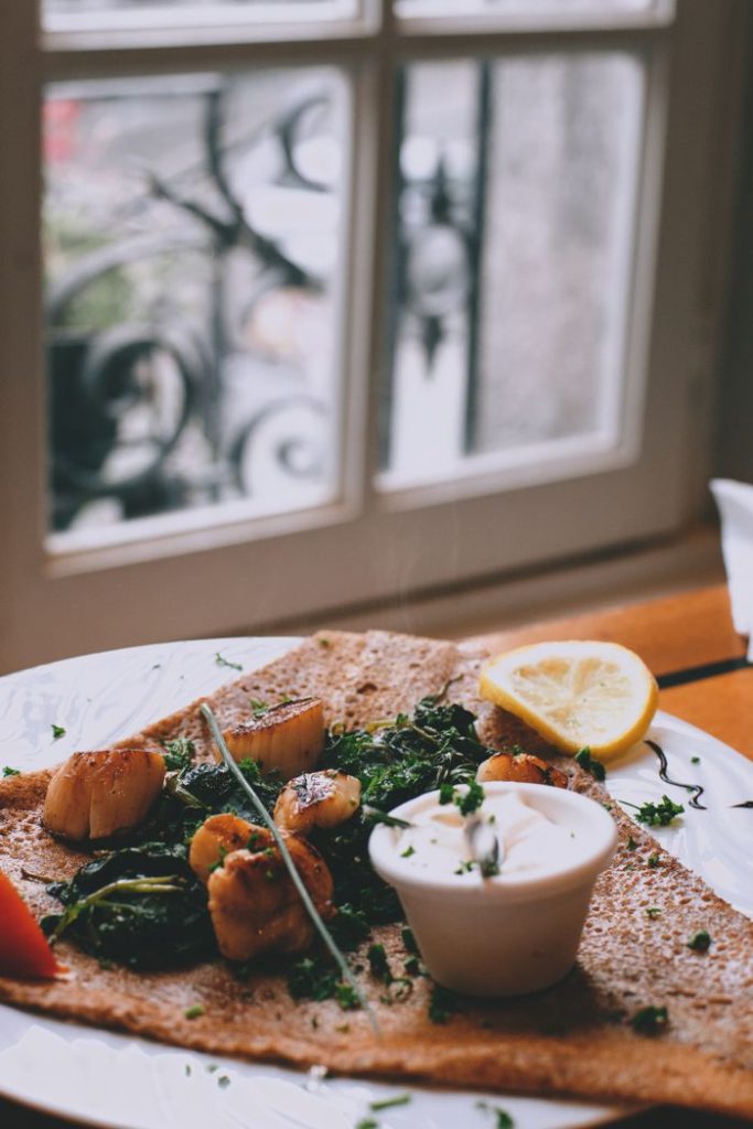 Delicious appetizing seared scallops with spinach served with sour cream and lemon slice on wooden table in seafood restaurant