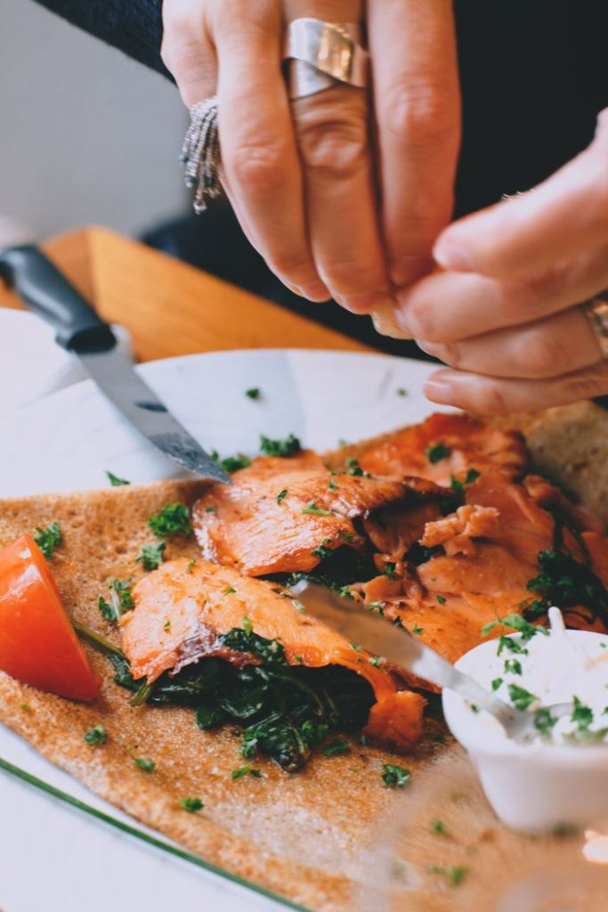 Crop unrecognizable female decorating yummy appetizing salmon with parsley and spring onions before serving for dinner